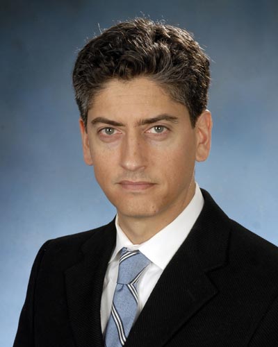 Photo of Brian Mathur, PhD, wearing a black suit, white shirt, and blue tie in front of a blue background