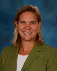 Jessica Mong, PhD is wearing a green blazer with a white blouse under it. She has shoulder length blonde hair and is smiling.