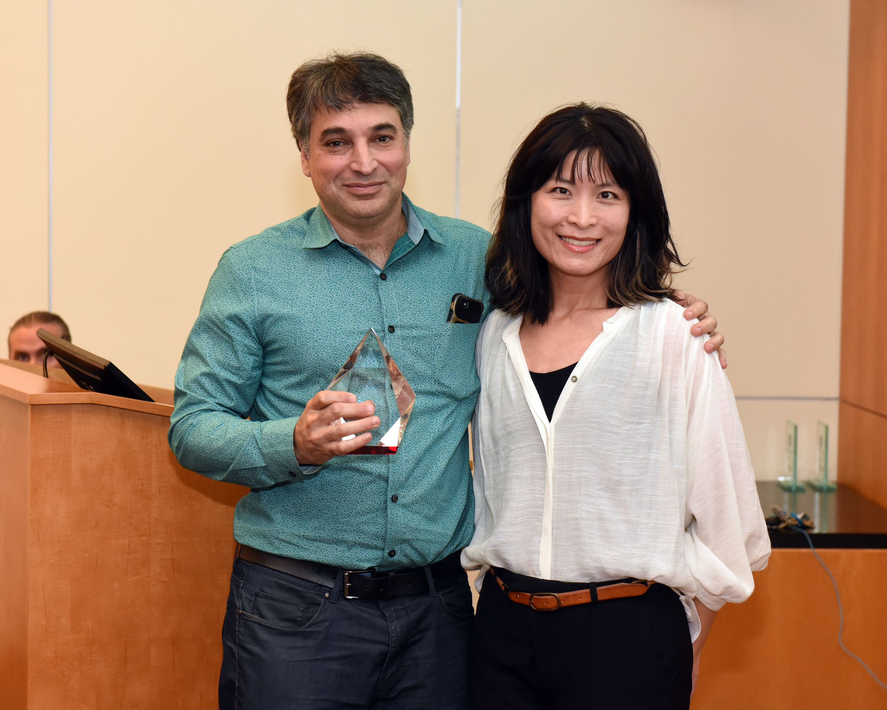 Dr. Mohammad Sajadi and Dr. Lydia Tang stand together. Dr. Mohammad Sajadi is holding his Faculty Excellence in Postdoctoral Mentorship Award