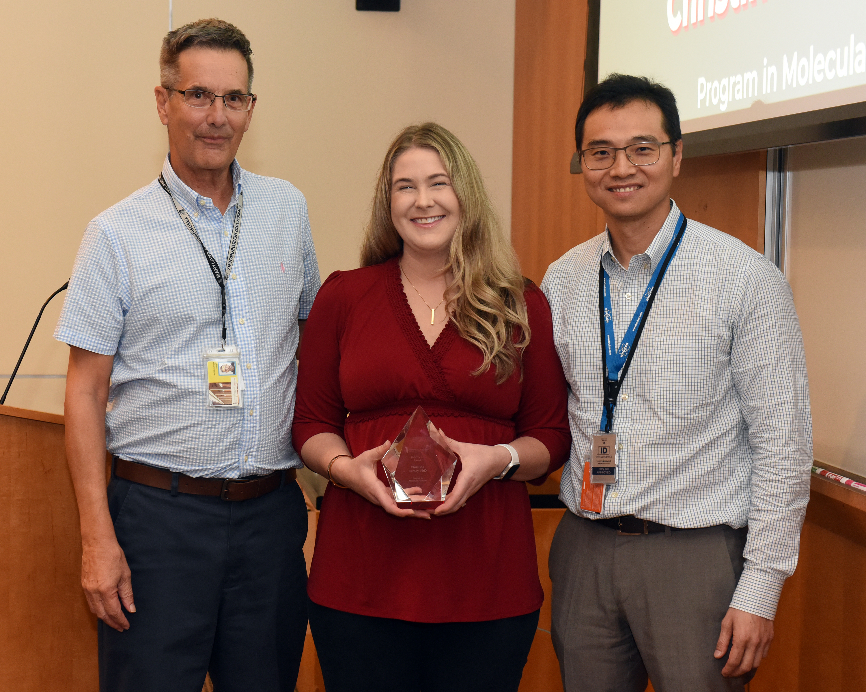 Dr. Jeff Winkles, Dr. Christine Carney, and Dr. Anthony Kim are standing together. Dr. Carney is holding her PhD Thesis Award.